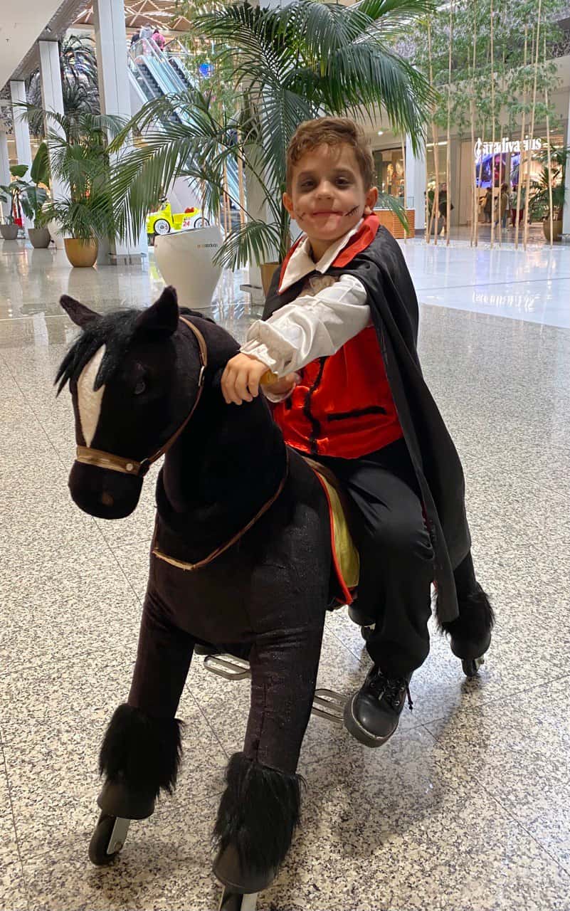 Un neno nun cabaliño negro xunto ás palmeiras do centro comercial