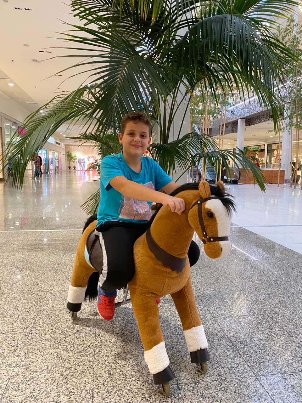 Un neno montado nun cabaliño marrón no centro comercial
